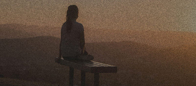 Silhouette of lady on bench watching the sunset over hills and mountainscape.