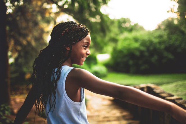 Medium shot of young girl outside stretching her arm out to someone off frame.