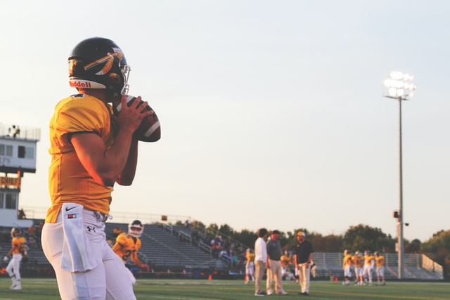 High school football player in orange jersey gets ready to launch a football on the field.